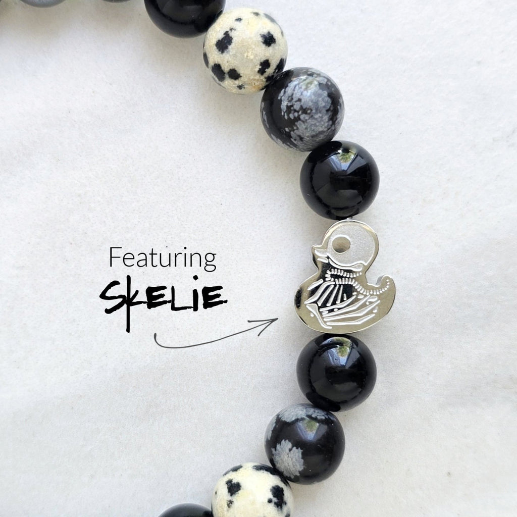 Beaded bracelet surrounded by decorative stones on a white background with 'Duck or Dare' text and brand names. Skelie duck for project fear dakota laden chelsea tanner alex