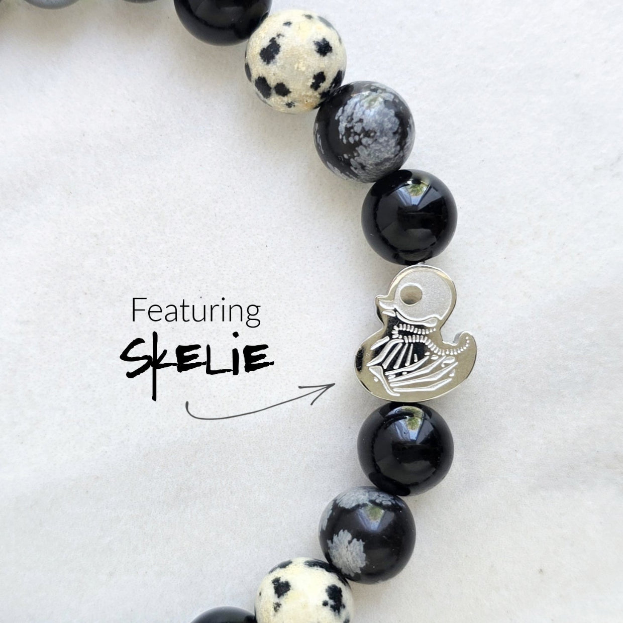 Beaded bracelet surrounded by decorative stones on a white background with 'Duck or Dare' text and brand names. Skelie duck for project fear dakota laden chelsea tanner alex