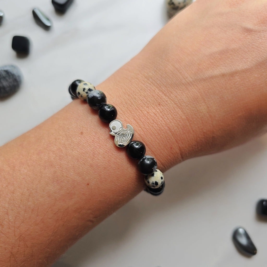 Beaded bracelet surrounded by decorative stones on a white background with 'Duck or Dare' text and brand names. Skelie duck for project fear dakota laden chelsea tanner alex