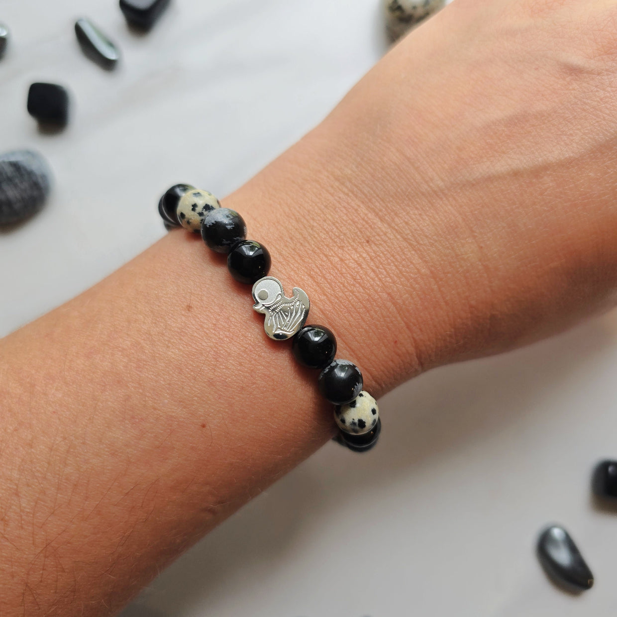 Beaded bracelet surrounded by decorative stones on a white background with 'Duck or Dare' text and brand names. Skelie duck for project fear dakota laden chelsea tanner alex