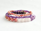 Set of beaded bracelets in pink, purple, and white on a light background