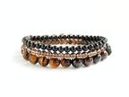 Stack of beaded bracelets with brown and black stones on a white background