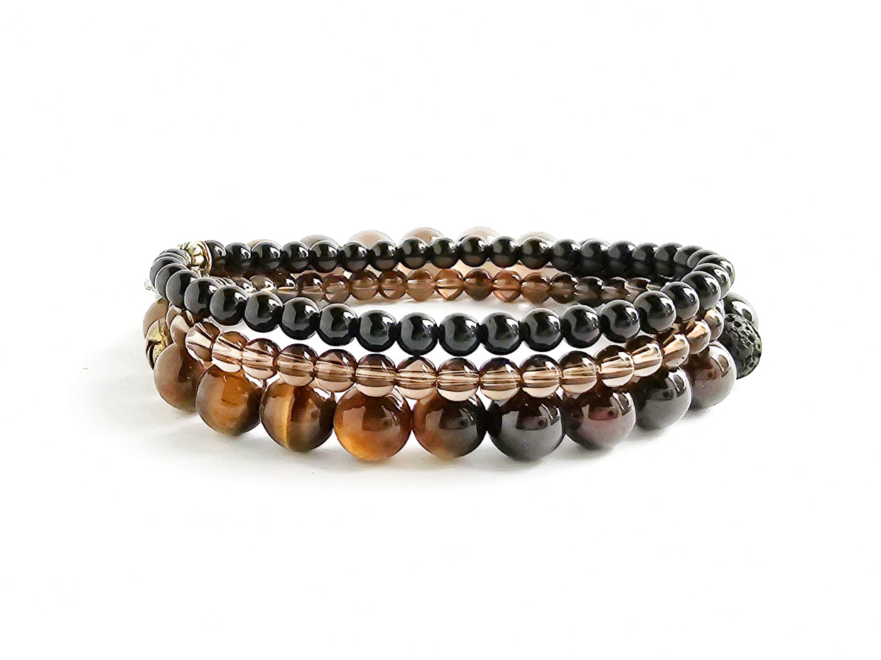 Stack of beaded bracelets with brown and black stones on a white background