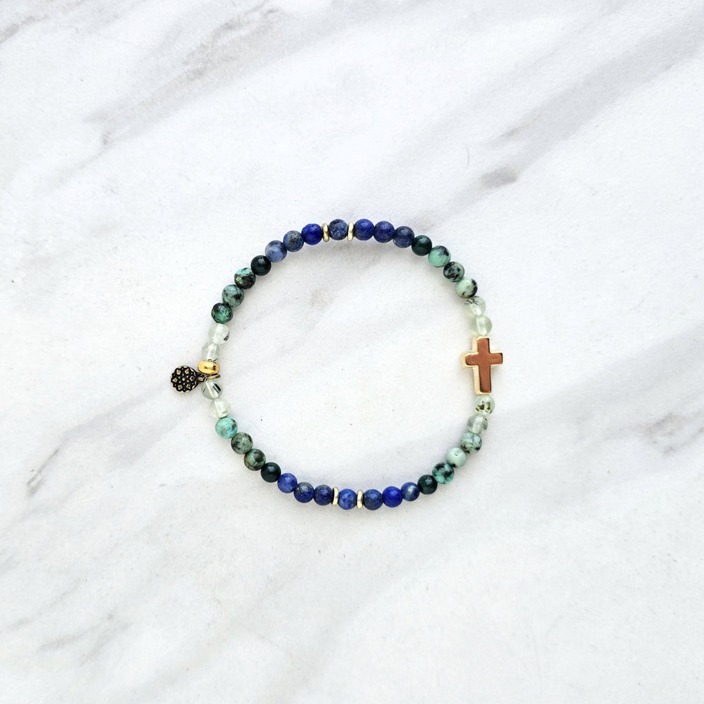 Beaded bracelet with a golden cross on a white marble background, featuring a quote from Proverbs 20:5. Christian Bracelet