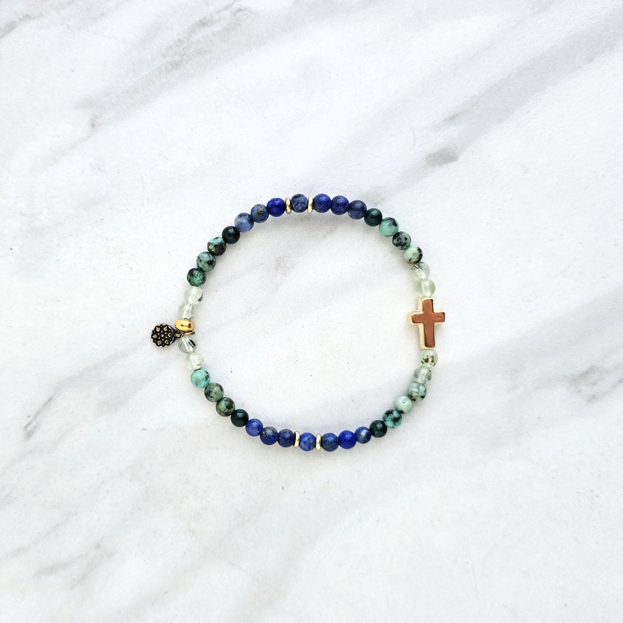 Beaded bracelet with a golden cross on a white marble background, featuring a quote from Proverbs 20:5. Christian Bracelet