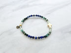 Beaded bracelet with a golden cross on a white marble background, featuring a quote from Proverbs 20:5. Christian Bracelet