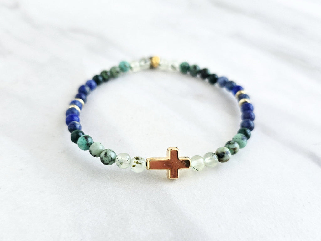 Beaded bracelet with a golden cross on a white marble background, featuring a quote from Proverbs 20:5. Christian Bracelet