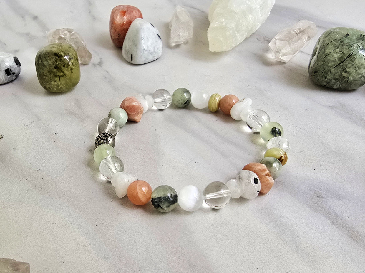 Crystal bracelet with stones on a marble surface, featuring 'Moxie Monthly' branding. The Calling June 2026