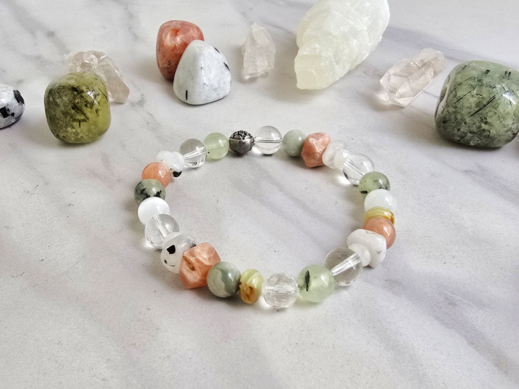 Crystal bracelet with stones on a marble surface, featuring 'Moxie Monthly' branding. June 2026 the calling