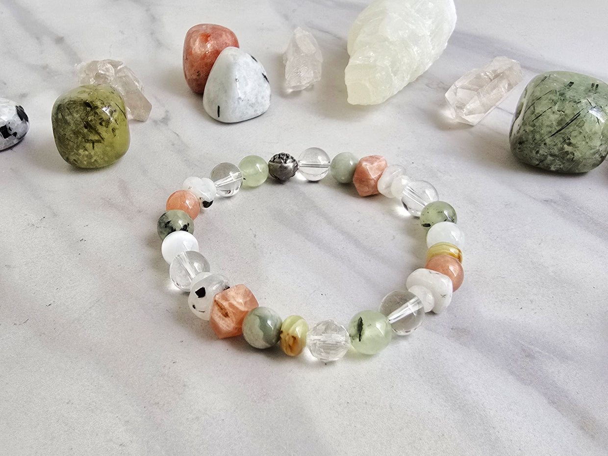 Crystal bracelet with stones on a marble surface, featuring 'Moxie Monthly' branding. June 2026 the calling