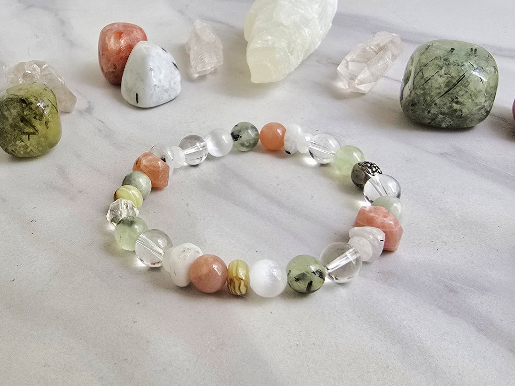 Crystal bracelet with stones on a marble surface, featuring 'Moxie Monthly' branding. The Calling June 2026