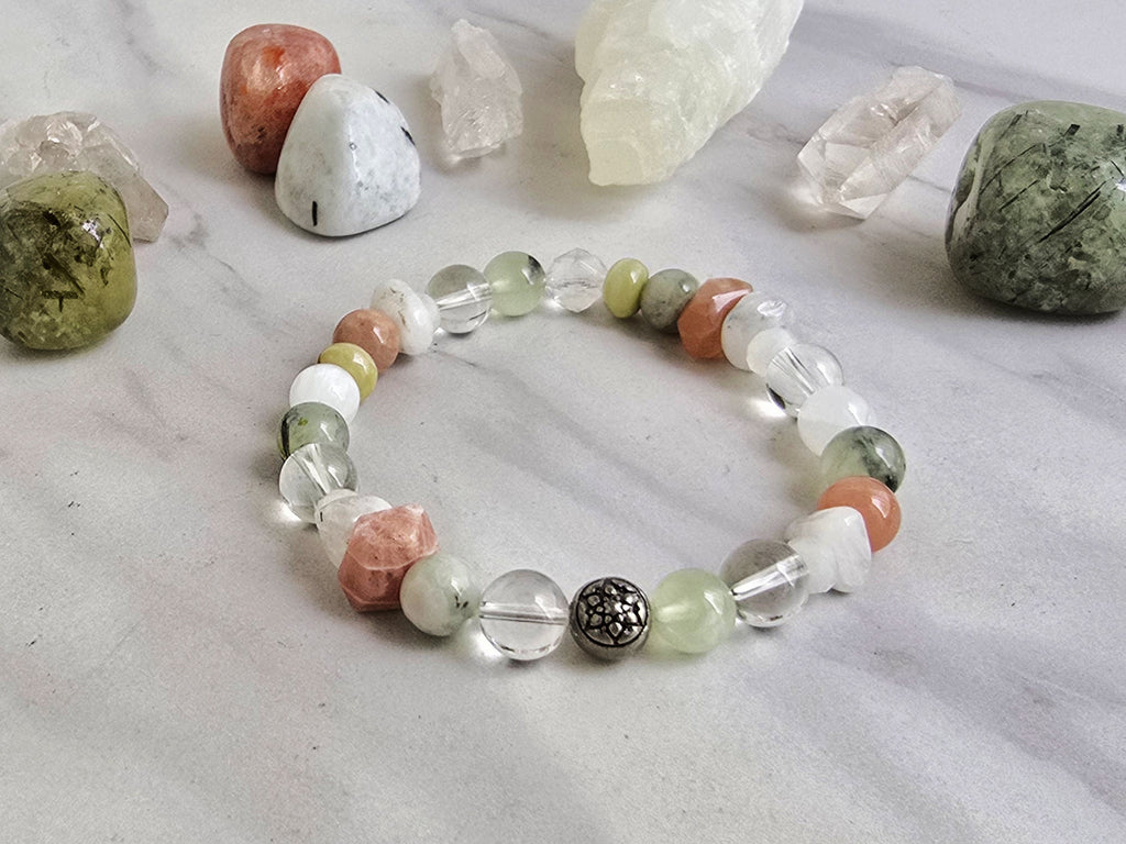 Crystal bracelet with stones on a marble surface, featuring 'Moxie Monthly' branding. June 2026 the calling