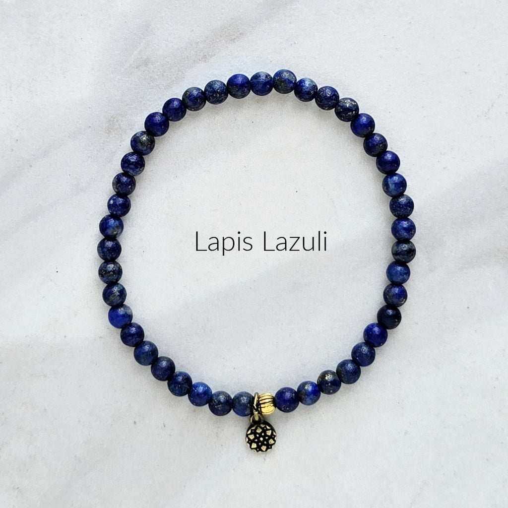 Lapis Lazuli beaded bracelet with a gold and black charm on a white marble background