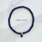Lapis Lazuli beaded bracelet with a gold and black charm on a white marble background