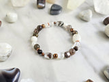 Bracelet with stones on a marble surface, featuring 'MOXIE Monthly' branding. open to receive brown white copper colors