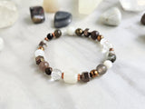 Bracelet with stones on a marble surface, featuring 'MOXIE Monthly' branding. open to receive brown white copper colors