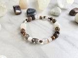 Bracelet with stones on a marble surface, featuring 'MOXIE Monthly' branding. open to receive brown white copper colors