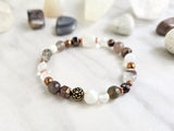 Bracelet with stones on a marble surface, featuring 'MOXIE Monthly' branding. open to receive brown white copper colors
