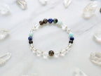 Bracelet with beads on a marble surface surrounded by crystal stones, featuring 'Sandalphon' and 'Archangel Collection'.