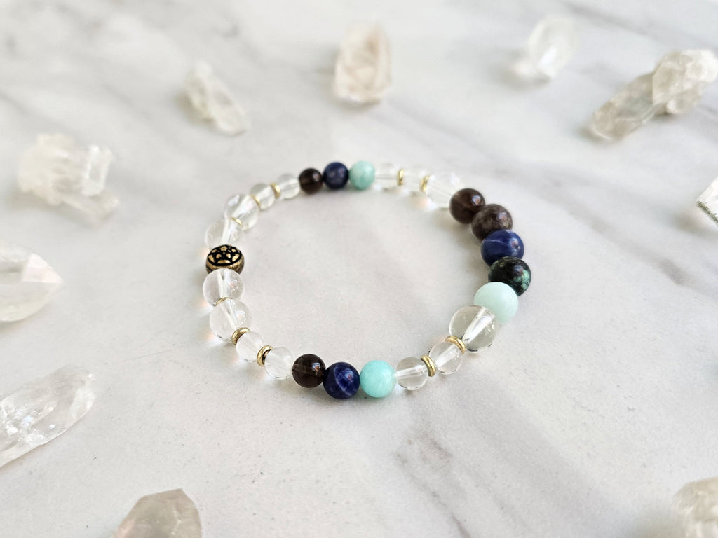 Bracelet with beads on a marble surface surrounded by crystal stones, featuring 'Sandalphon' and 'Archangel Collection'.