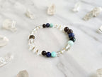Bracelet with beads on a marble surface surrounded by crystal stones, featuring 'Sandalphon' and 'Archangel Collection'.