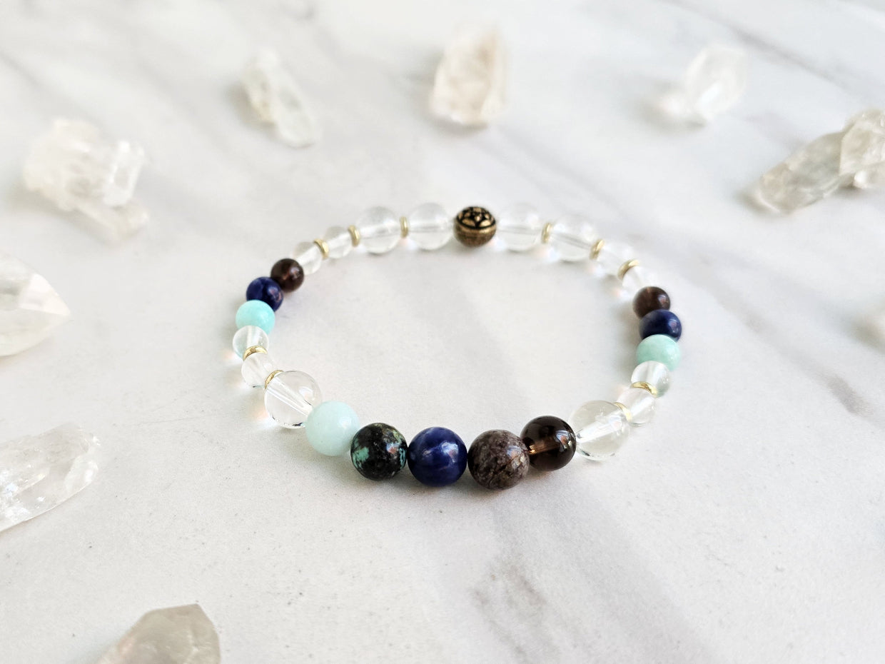 Bracelet with beads on a marble surface surrounded by crystal stones, featuring 'Sandalphon' and 'Archangel Collection'.