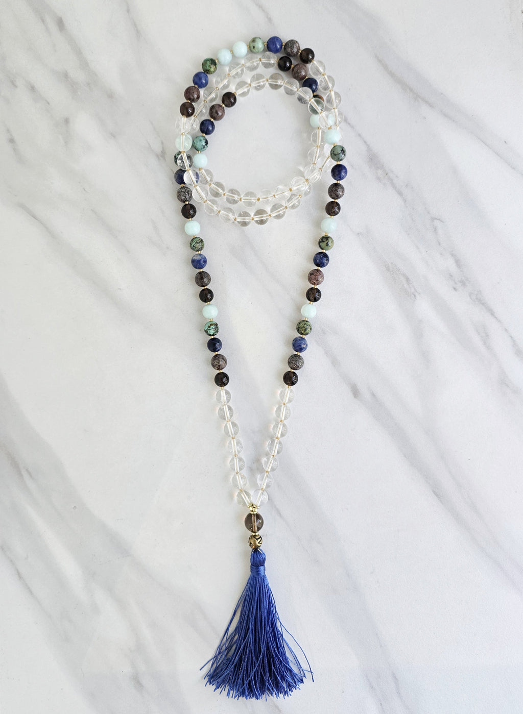 Beaded necklace with a blue tassel on a white marble surface sandalphon meditation beads mala