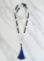 Beaded necklace with a blue tassel on a white marble surface sandalphon meditation beads mala
