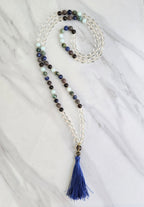 Beaded necklace with a blue tassel on a white marble surface sandalphon meditation beads mala