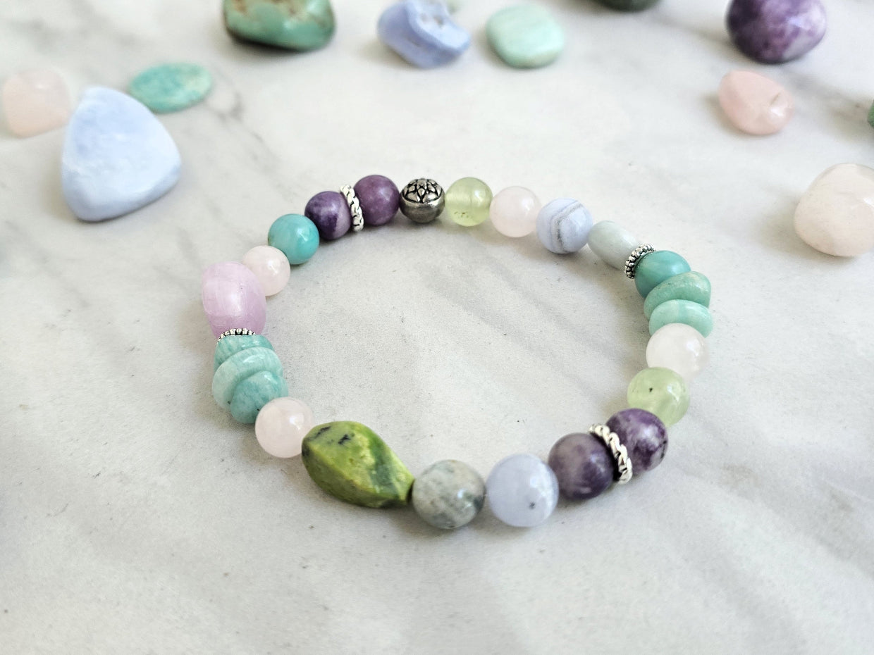 A beaded bracelet with pastel and earthy tones is arranged on a light marble surface, surrounded by polished crystals. Text overlays read 'MOXIE Monthly', 'Joyful Service', and 'September 2026'.