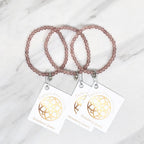 Two strawberry quartz beaded bracelets with matching tags on a marble surface. valentines day galentines gifts