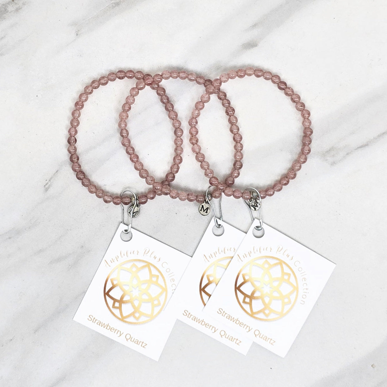 Two strawberry quartz beaded bracelets with matching tags on a marble surface. valentines day galentines gifts