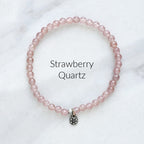 Pink beaded bracelet with a silver charm on a white marble background, labeled 'Strawberry Quartz'.